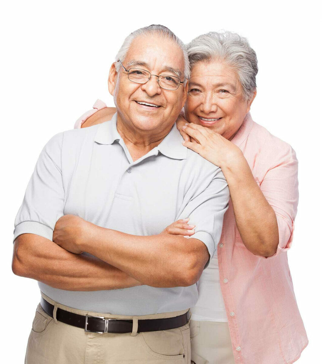Mature couple smiling at camera. Man standing in front with arms crossed, woman behind him with with head and hands resting on his shoulder.